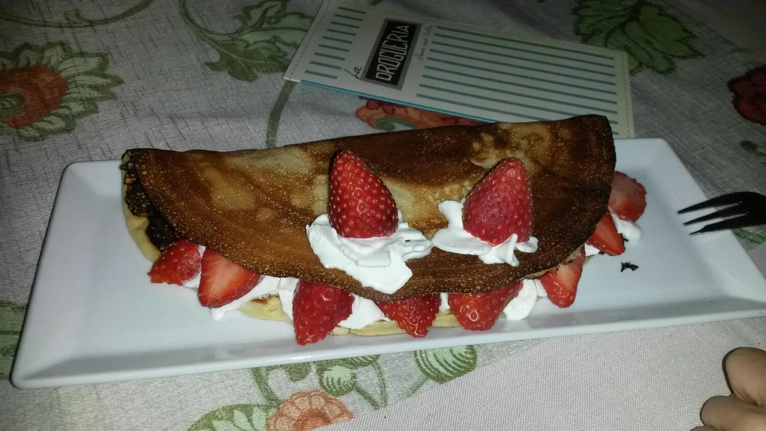 Crepe dulce con fresas y crema batida, servido en un plato blanco. Ideal para un postre delicioso.