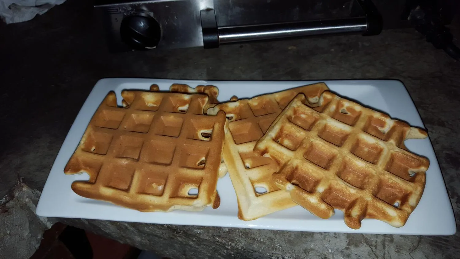 Tres waffles dorados y crujientes servidos en un plato blanco, listos para disfrutar. Ideal para el desayuno o como un delicioso postre.