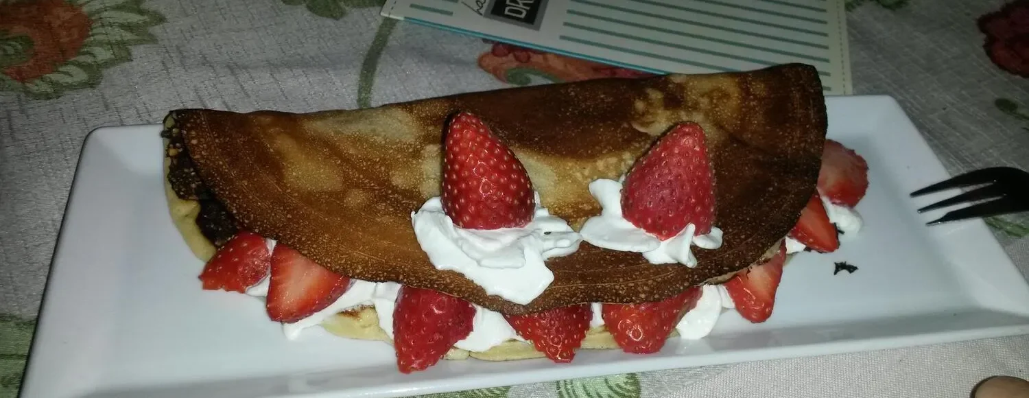 Crepe dulce con fresas y crema batida, servido en un plato blanco. Ideal para un postre delicioso.